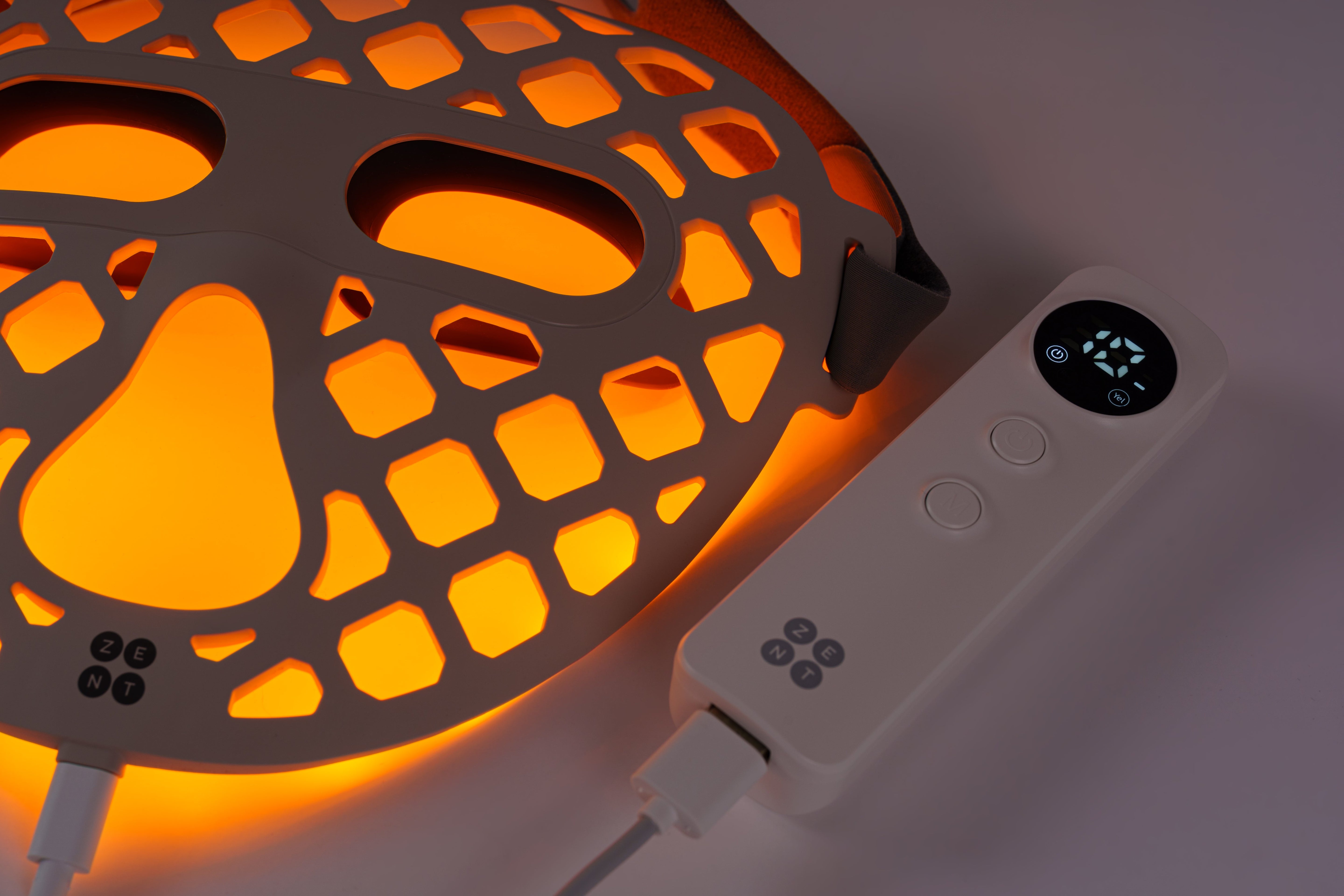 ZENT® DermaLight™ – Inteligentna maska LED do fototerapii 4w1 w trybie żółtego światła. Obok leży pilot sterujący