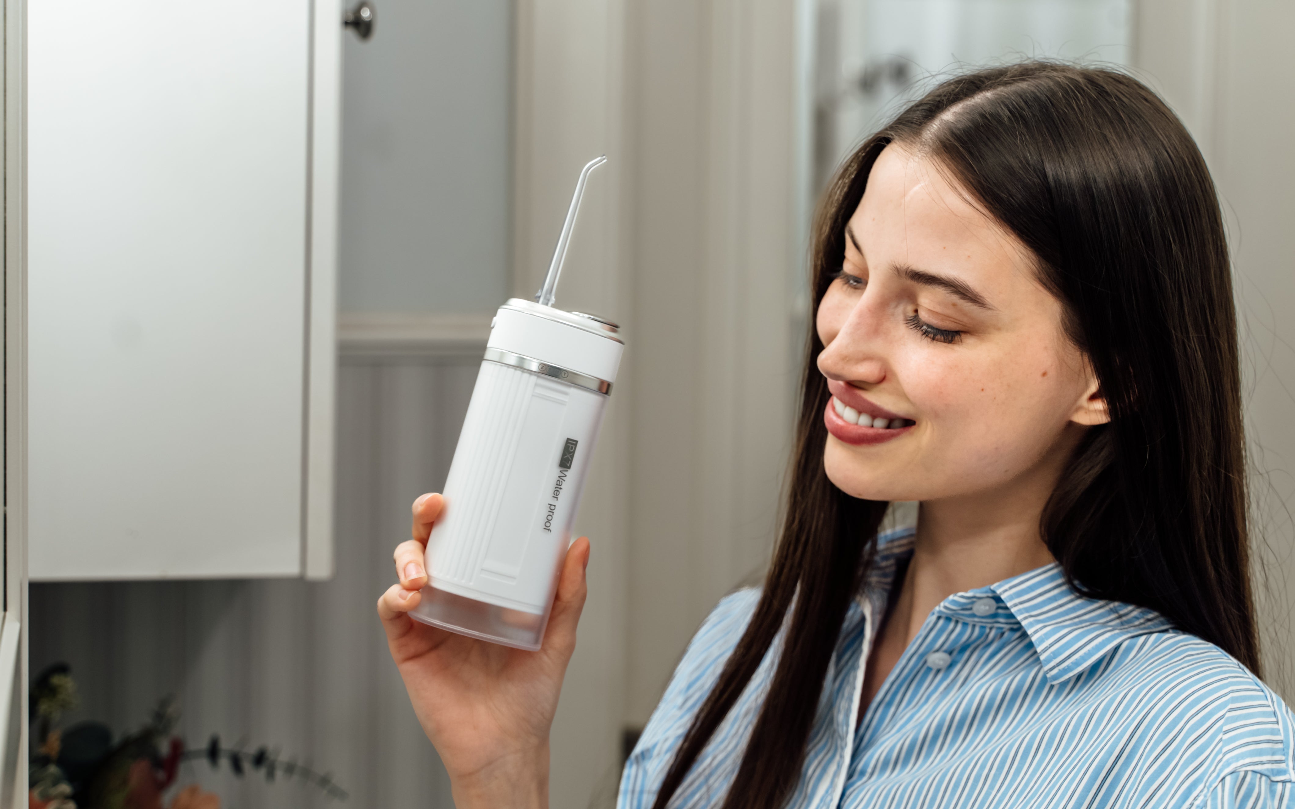 Uśmiechnięta kobieta trzyma w ręku ZENT® Stream+ Irygator stomatologiczny do zębów