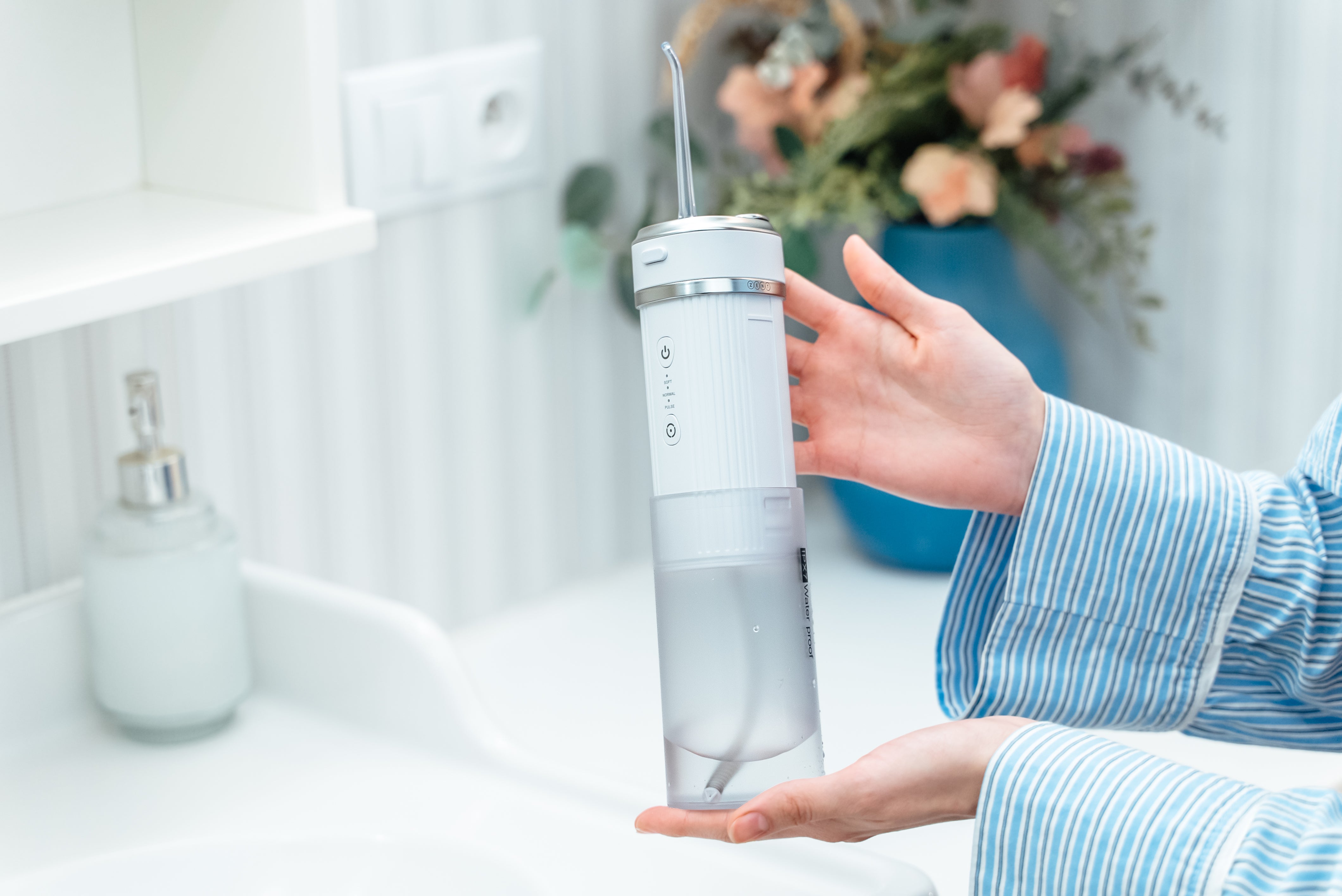 Na zdjęciu kobiece ręce trzymające w łazience Irygator stomatologiczny do zębów ZENT® Stream+