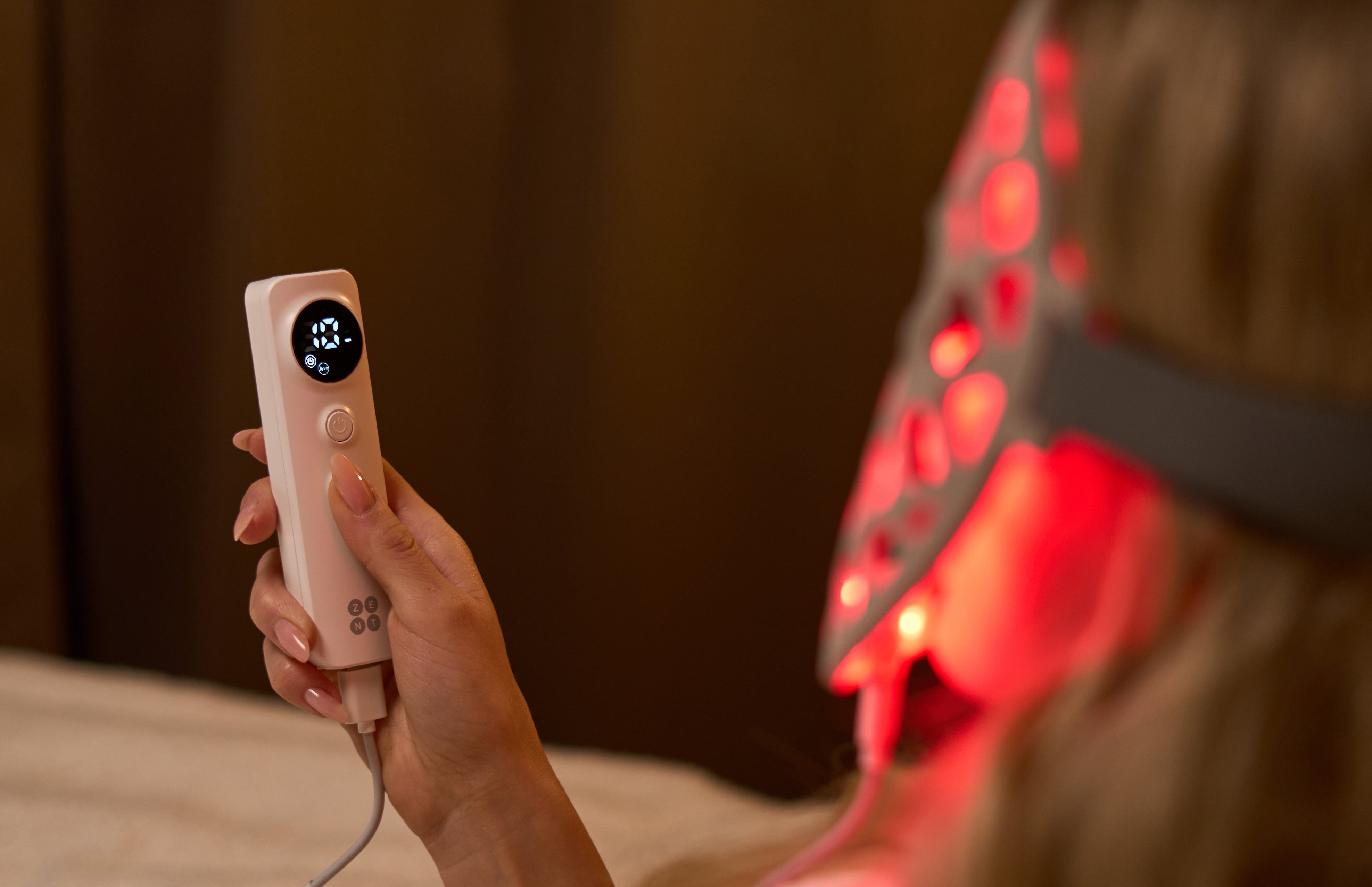 ZENT® DermaLight™ – Inteligentna maska LED do fototerapii 4w1 na twarzy kobiety, która trzyma w dłoni pilot sterujący