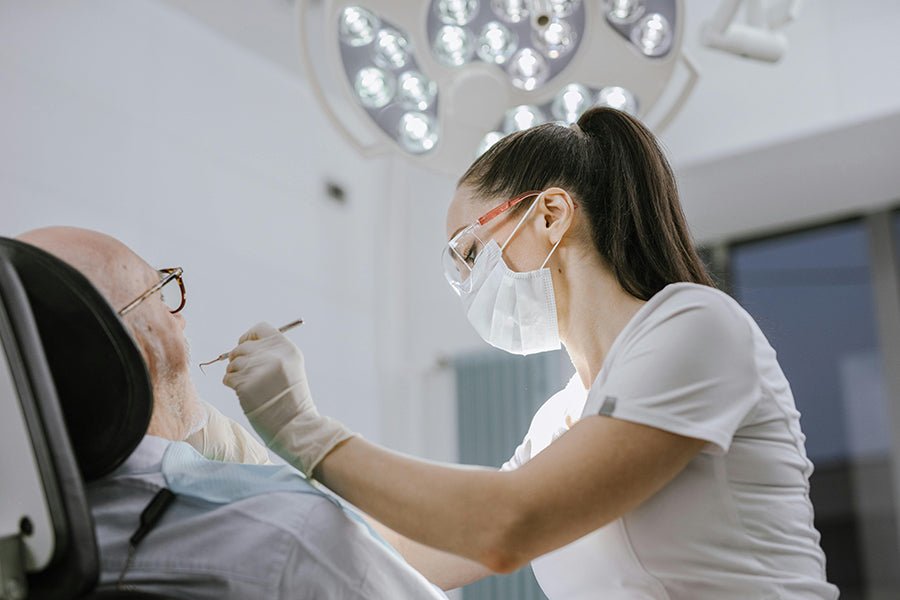 Dentystka sprawdza na fotelu stomatologicznym uzębienie starszego mężczyzny. Jakie zabiegi na NFZ za darmo?